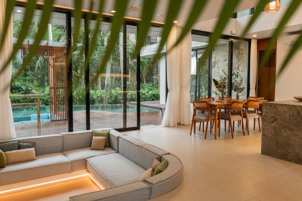 Private living room and dining area seen through tropical palms at Hubuddha Three Bedroom Villa Ubud Bali